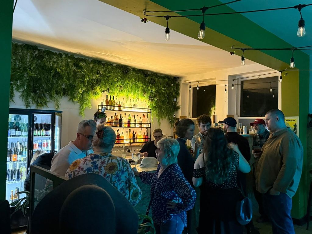 The Taproom bar at The Bach, lit spirits shelves under hanging ferns, busy with people